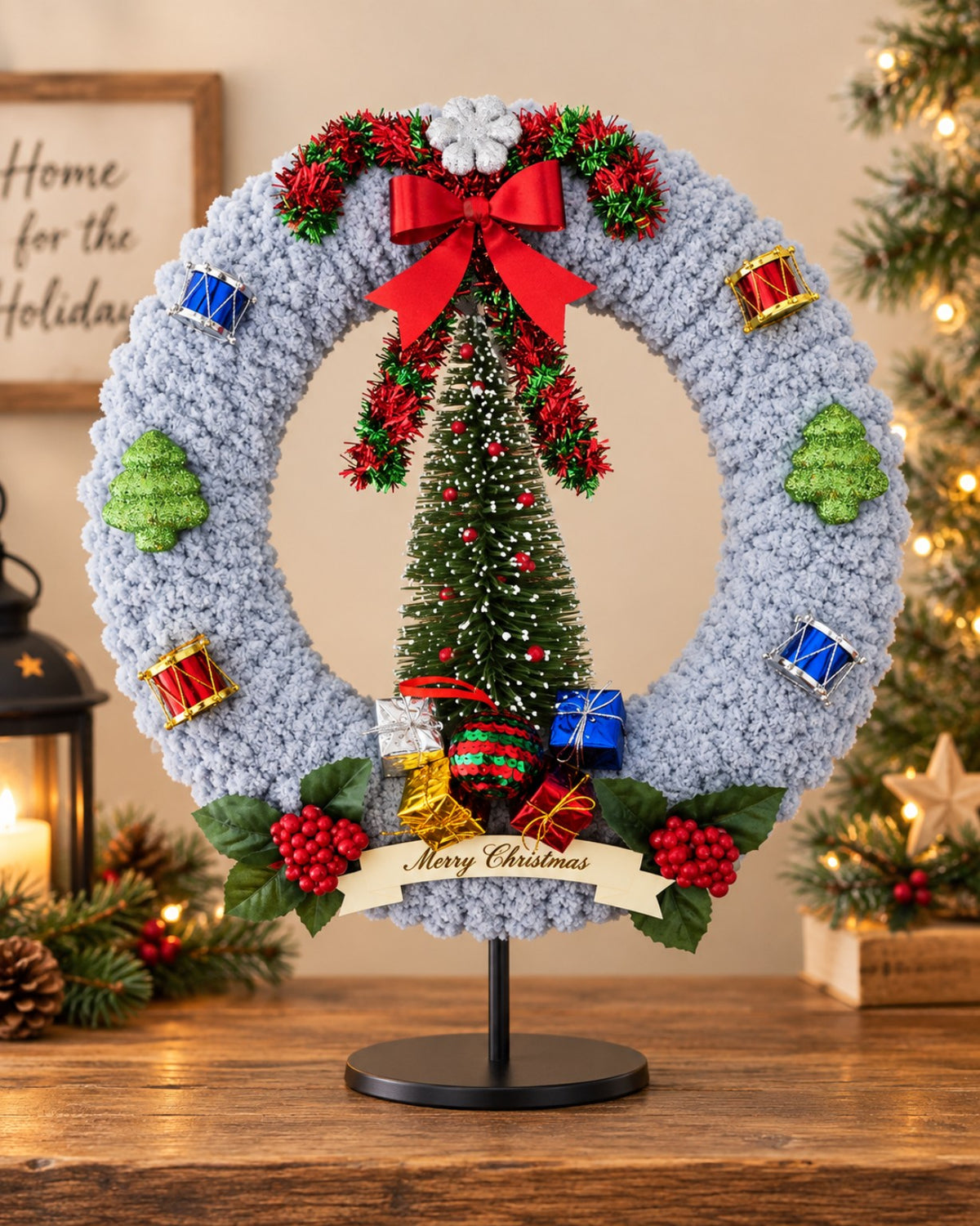 Handcrafted gray Christmas wreath with tree centerpiece, red bow, drums, wrapped gifts, holly berries and Merry Christmas banner
